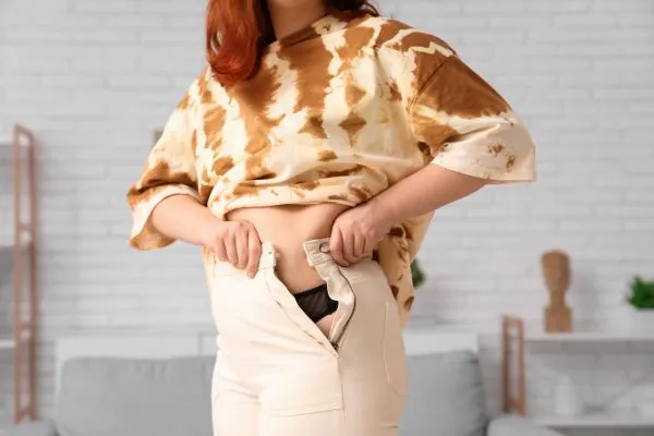 Image of woman trying to do her trousers up after pregnancy weight gain Hayes